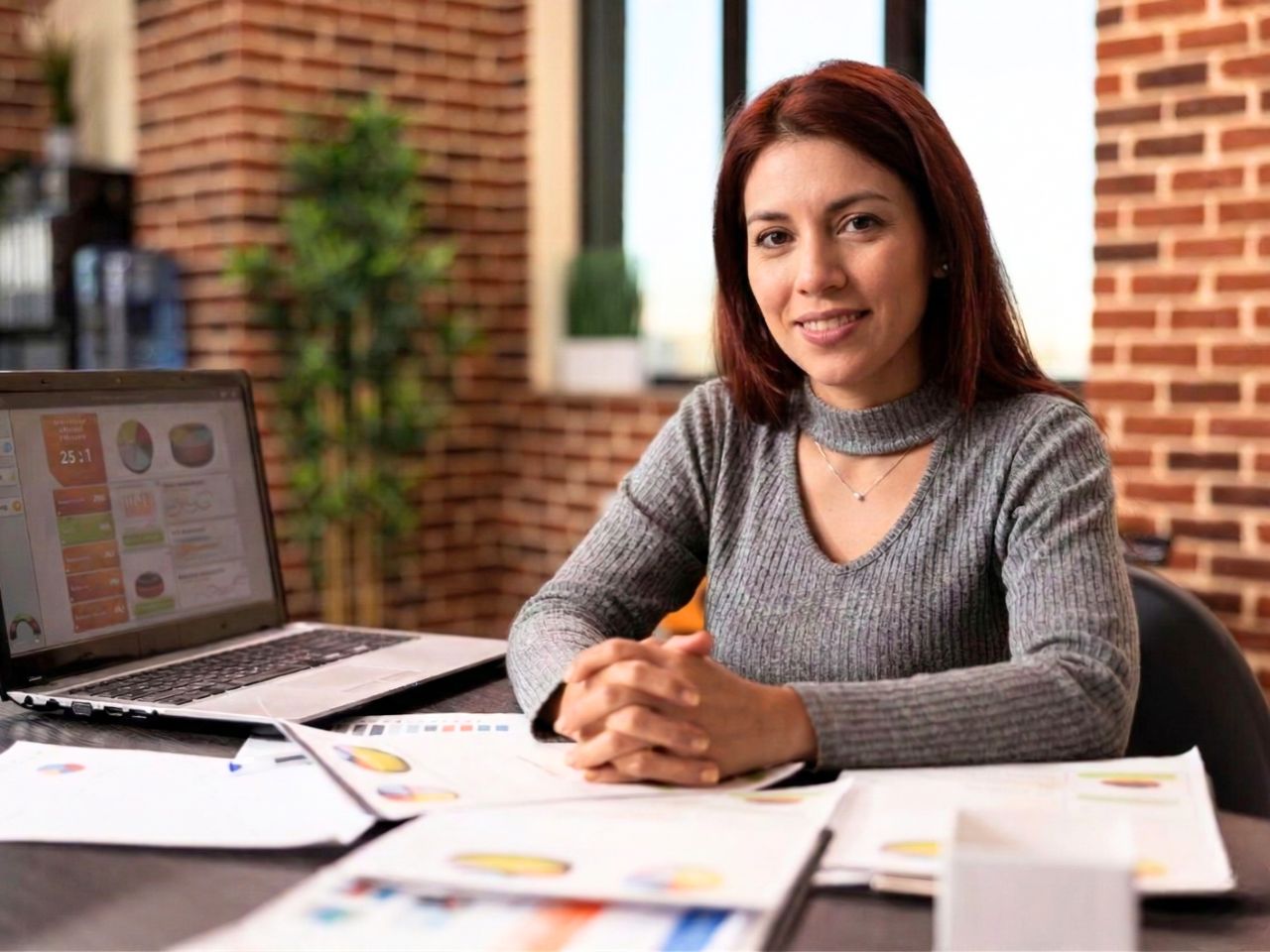 remote marketer smiling at her desk with a laptop and data charts