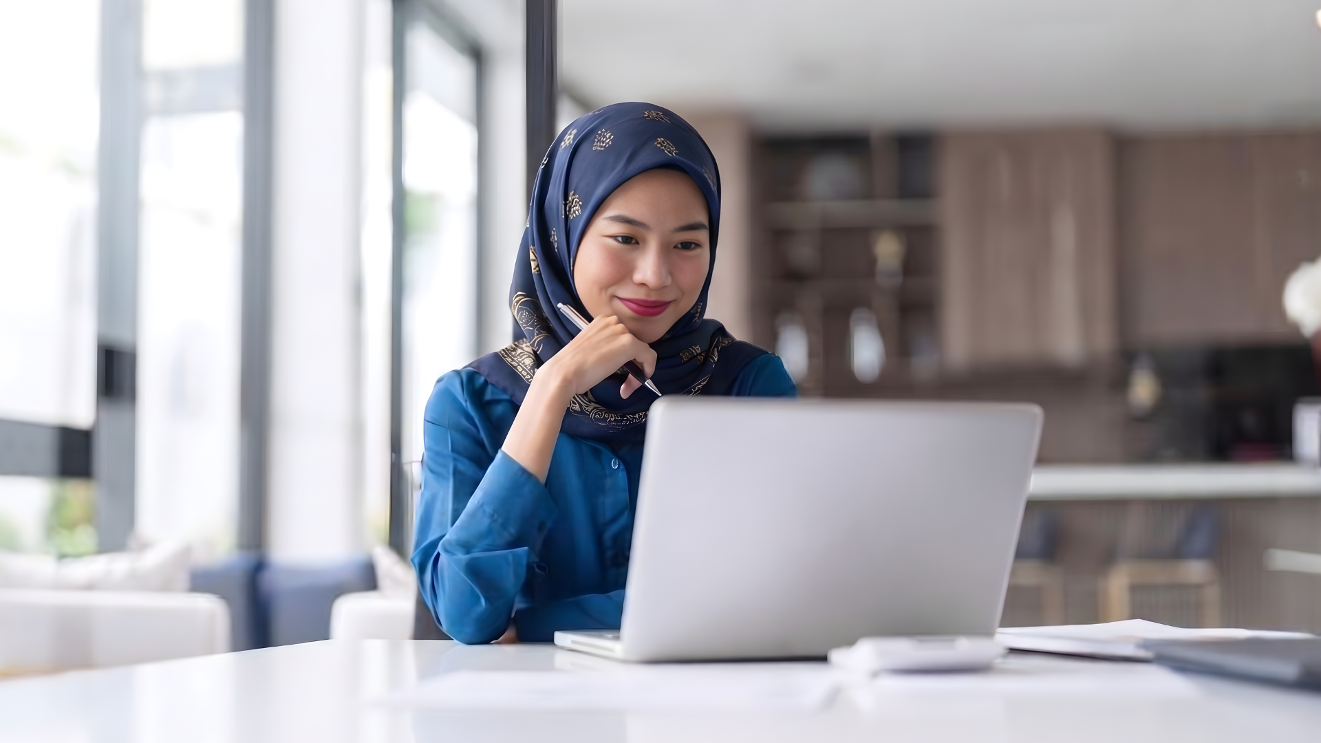 malaysian remote operations manager working with a laptop while holding a pen