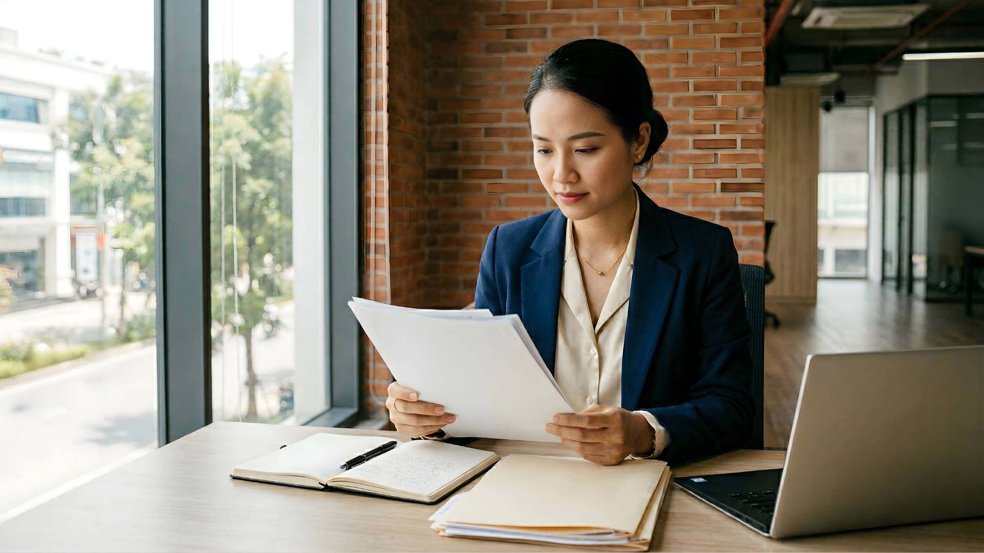 vietnamese remote compliance officer reading a contract with a pile of document and laptop on a desk