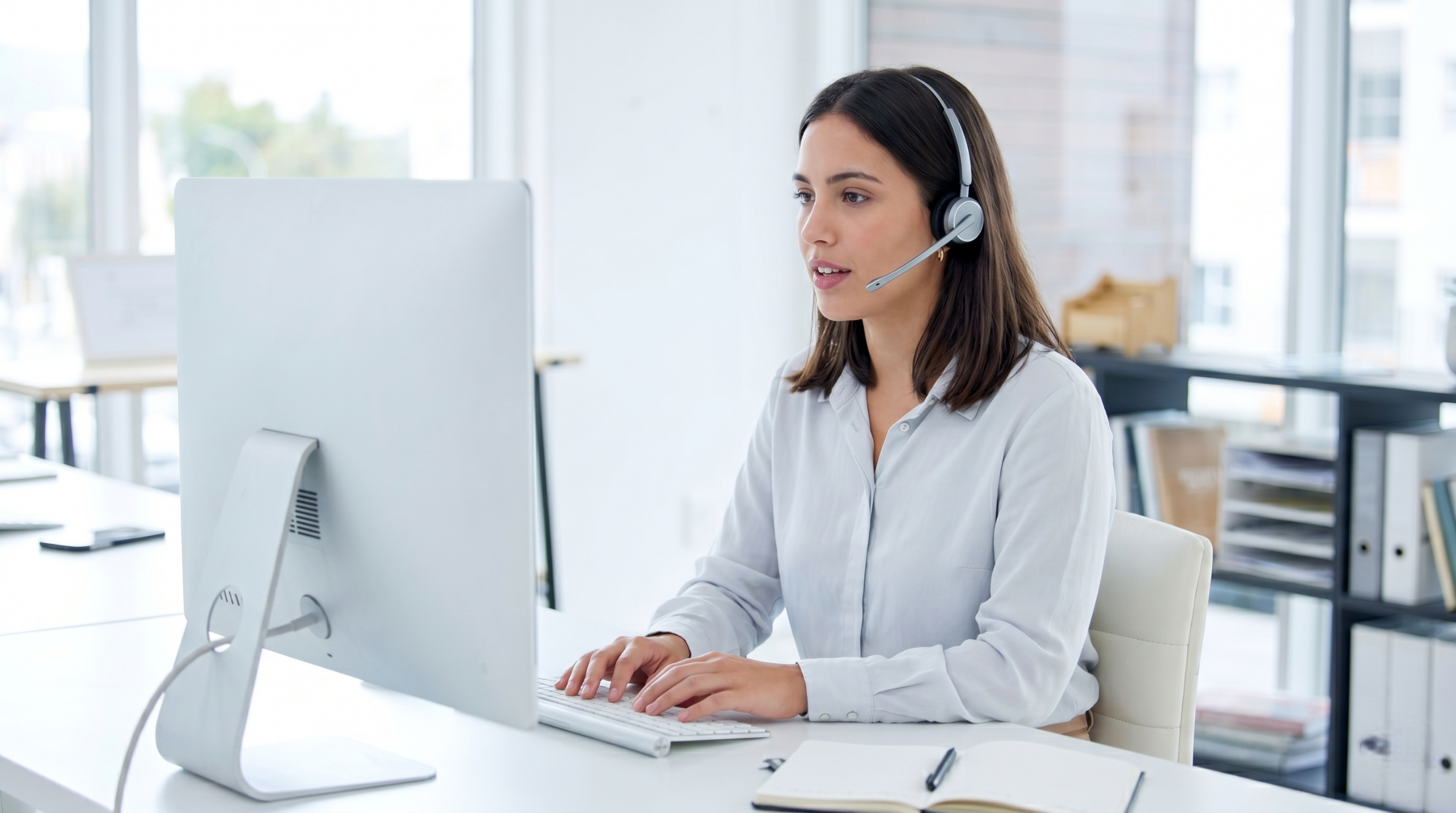 professional remote help desk support specialist talking into her headset while typing on a desktop computer