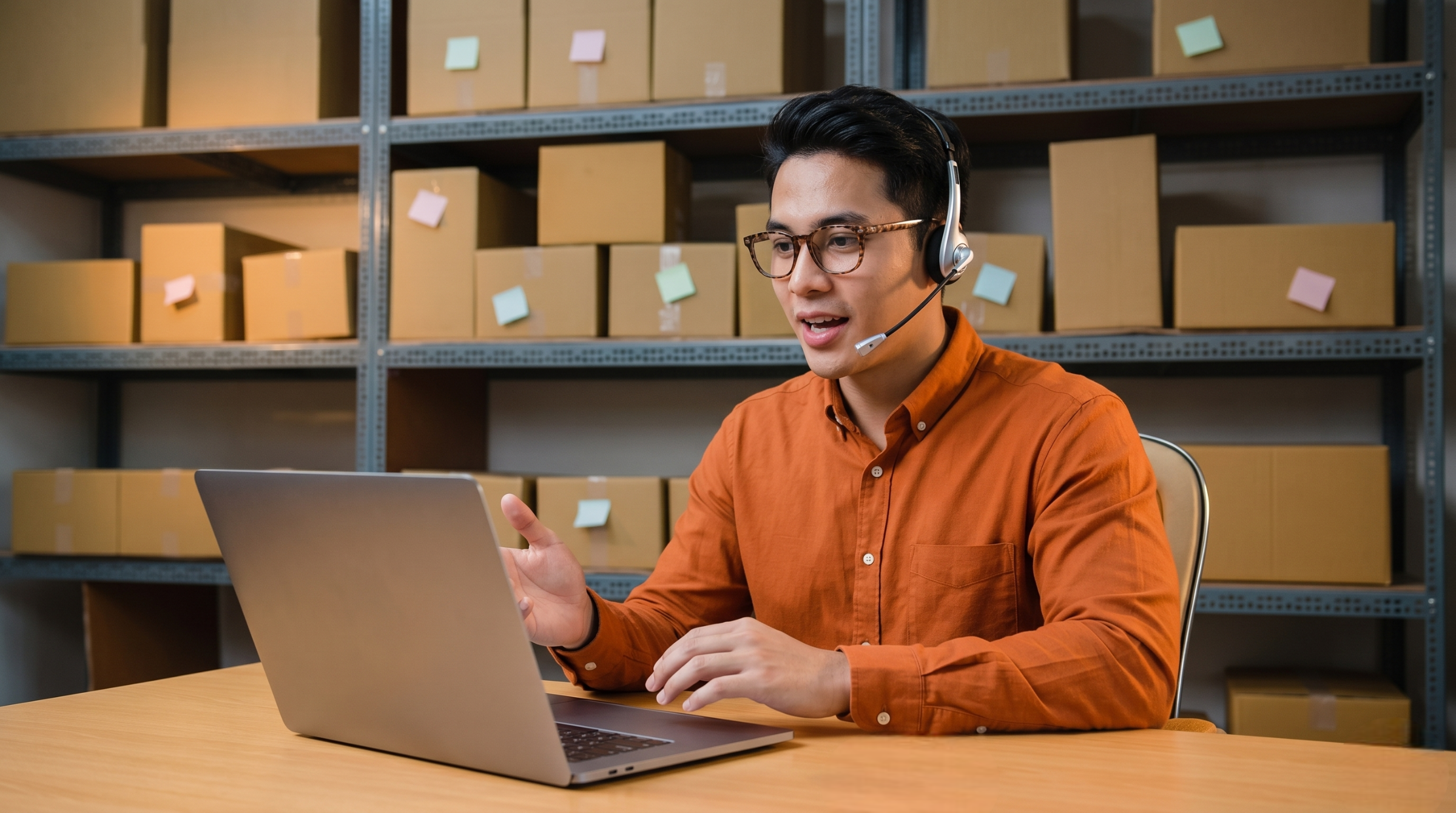 an outsourced logistics coordinator in Malaysia wearing glasses and a headset while tracking shipments on a laptop