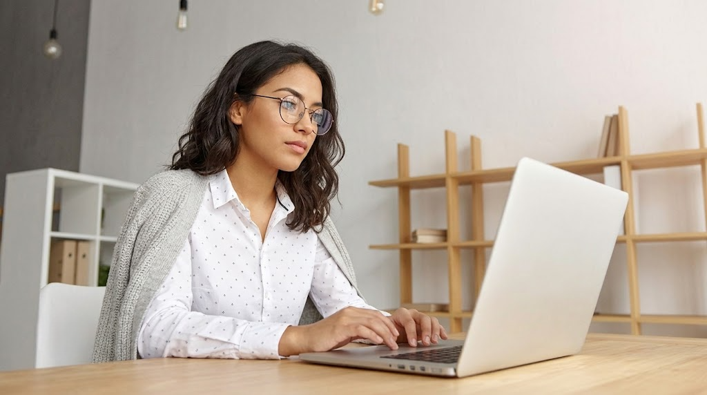 an outsource payroll officer wearing glasses and typing on a laptop from home