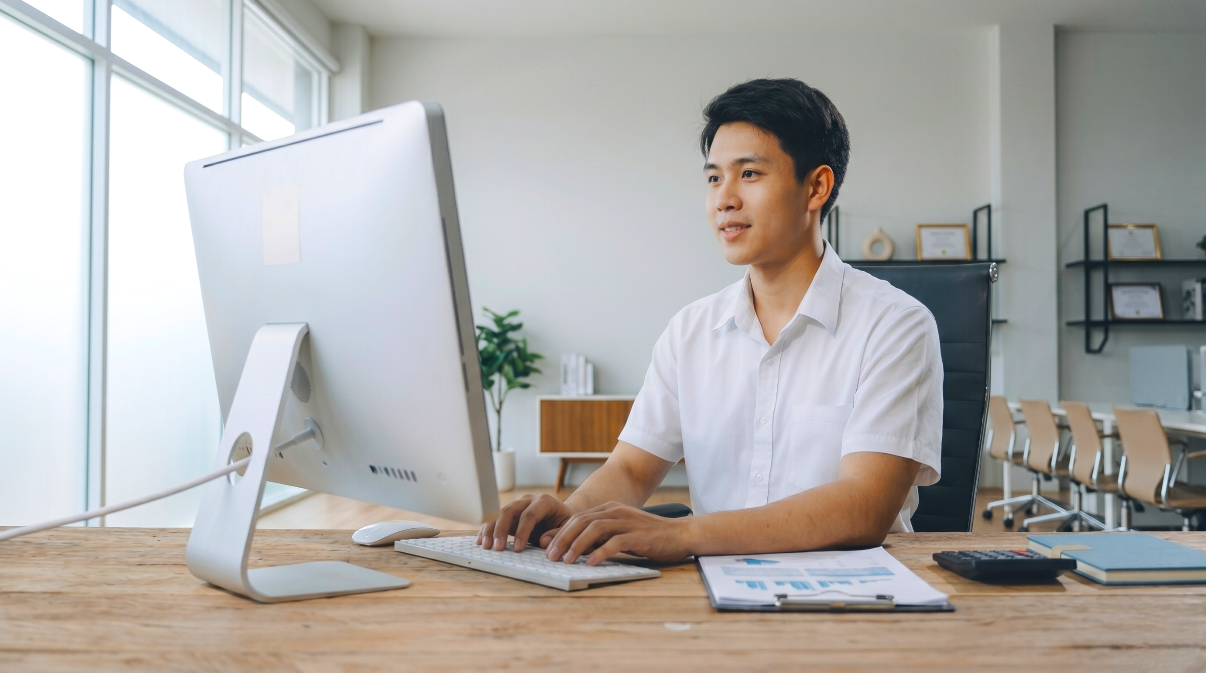 professional male remote supply chain planner in Vietnam working on a desktop computer in a bright, modern office space