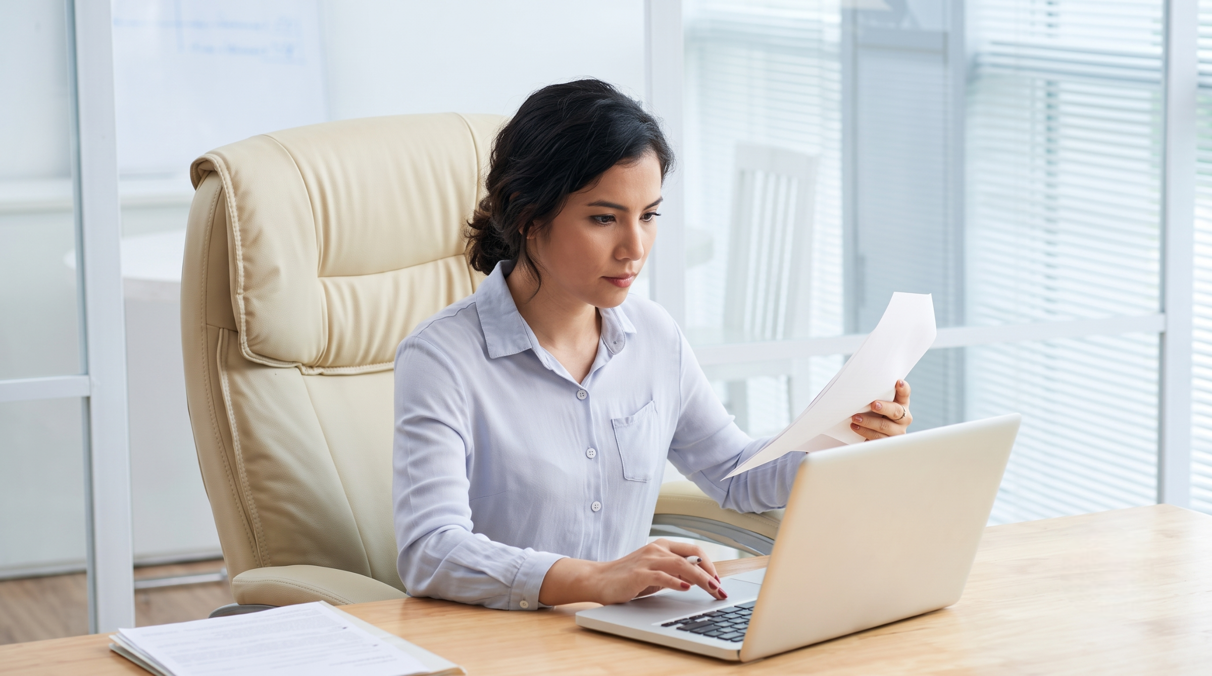 A remote payroll officer reviewing documents while working on her laptop in an office