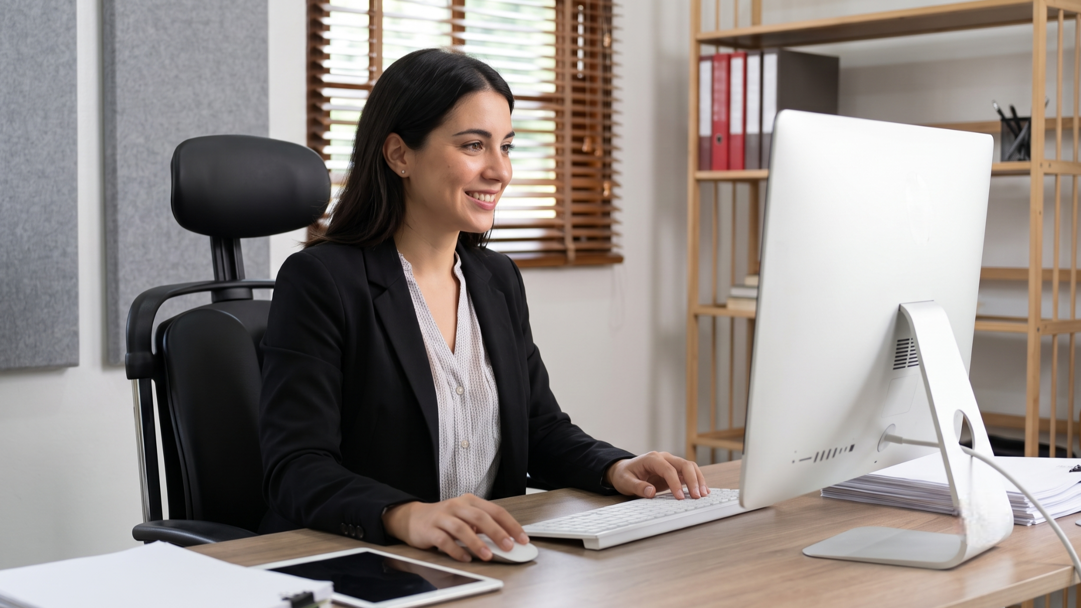 smiling outsourced accounting manager in a black blazer working on a desktop computer in an Argentina corporate office