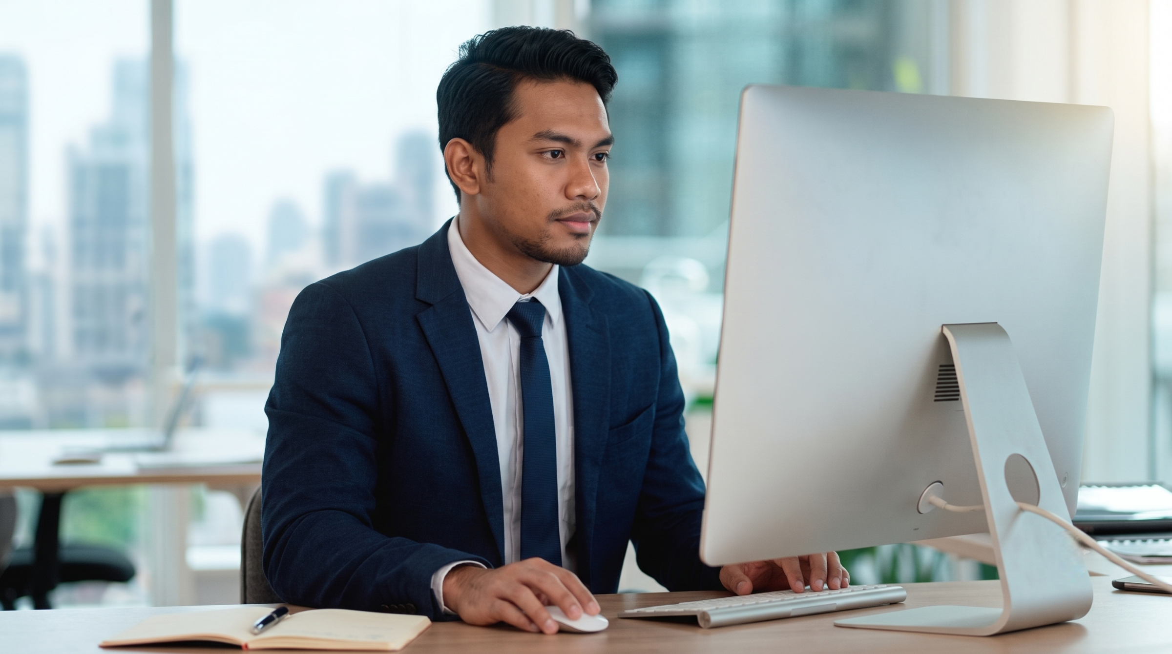 professional remote accounting manager sitting at an office desk working on a desktop computer with a city view in Malaysia