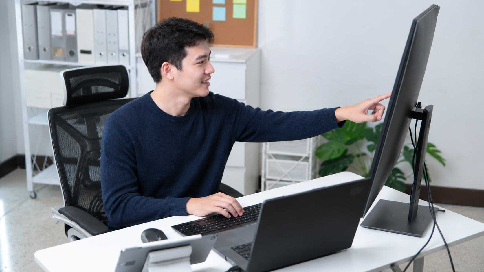 Asian male professional pointing at dual monitors, representing a remote bim coordinator working on 3D modeling