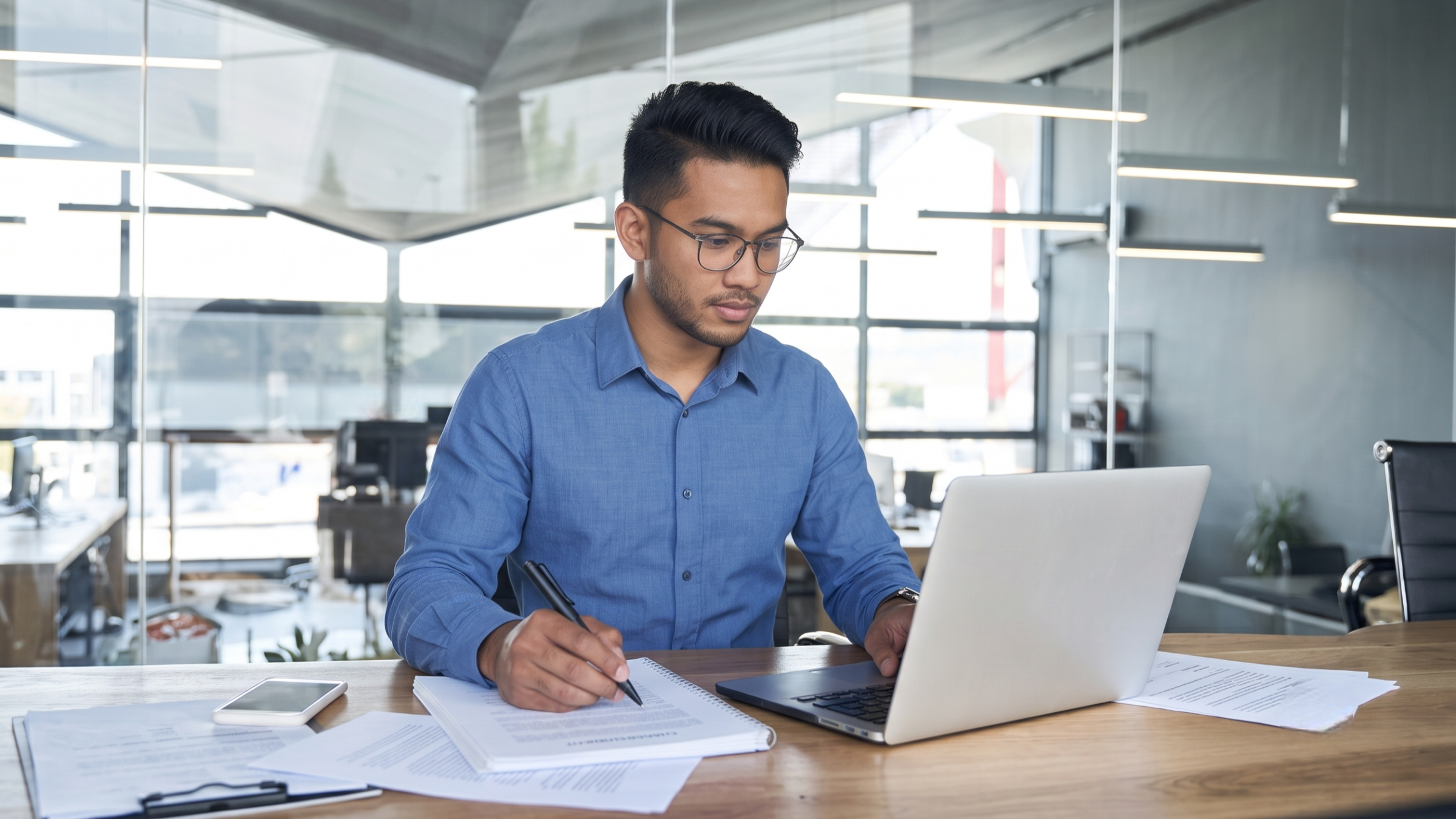 Professional contract administrator remote working on a laptop and reviewing documents at a modern office desk in Malaysia