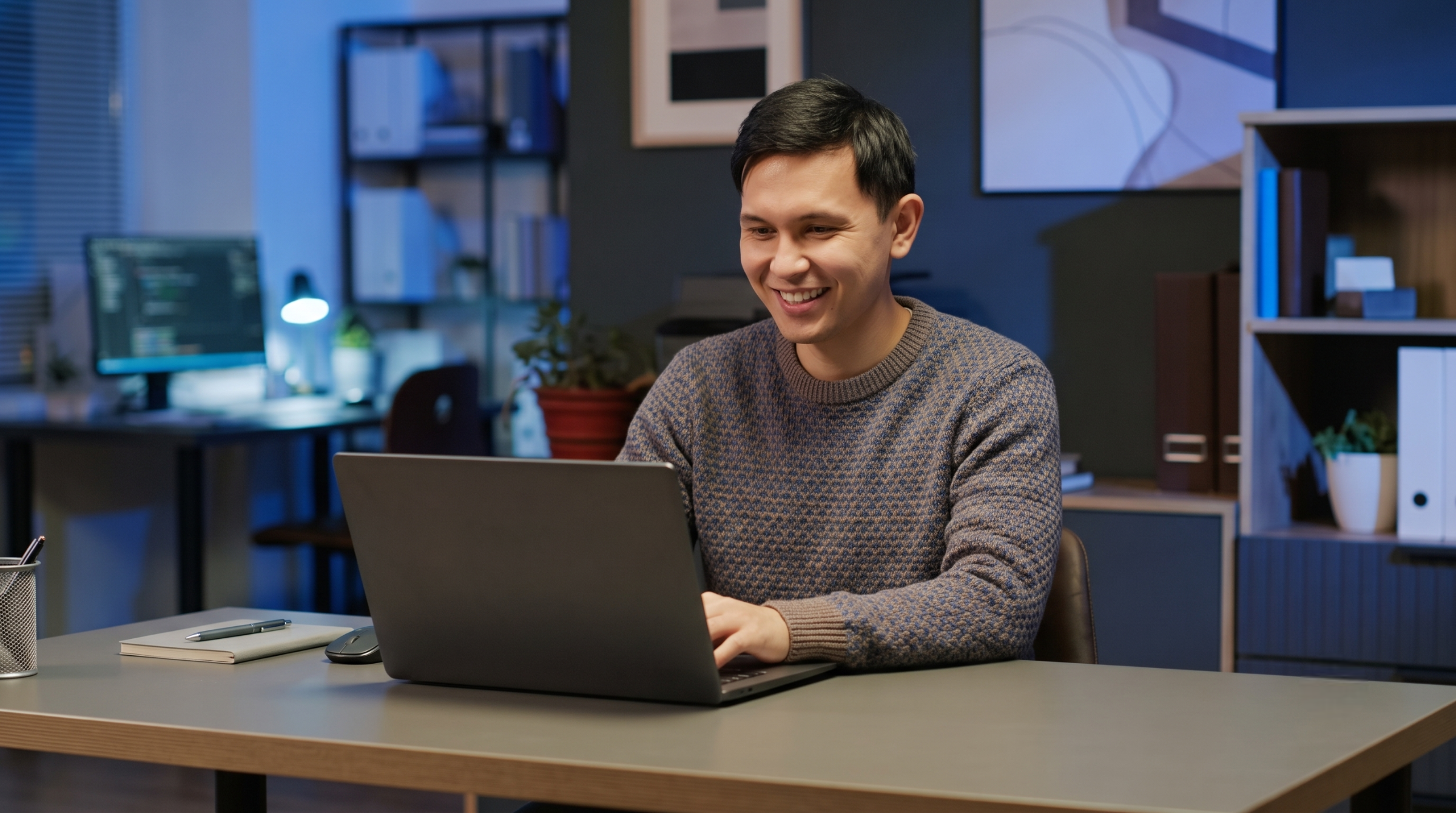 remote cyber security engineer working on laptop at desk in evening office setup
