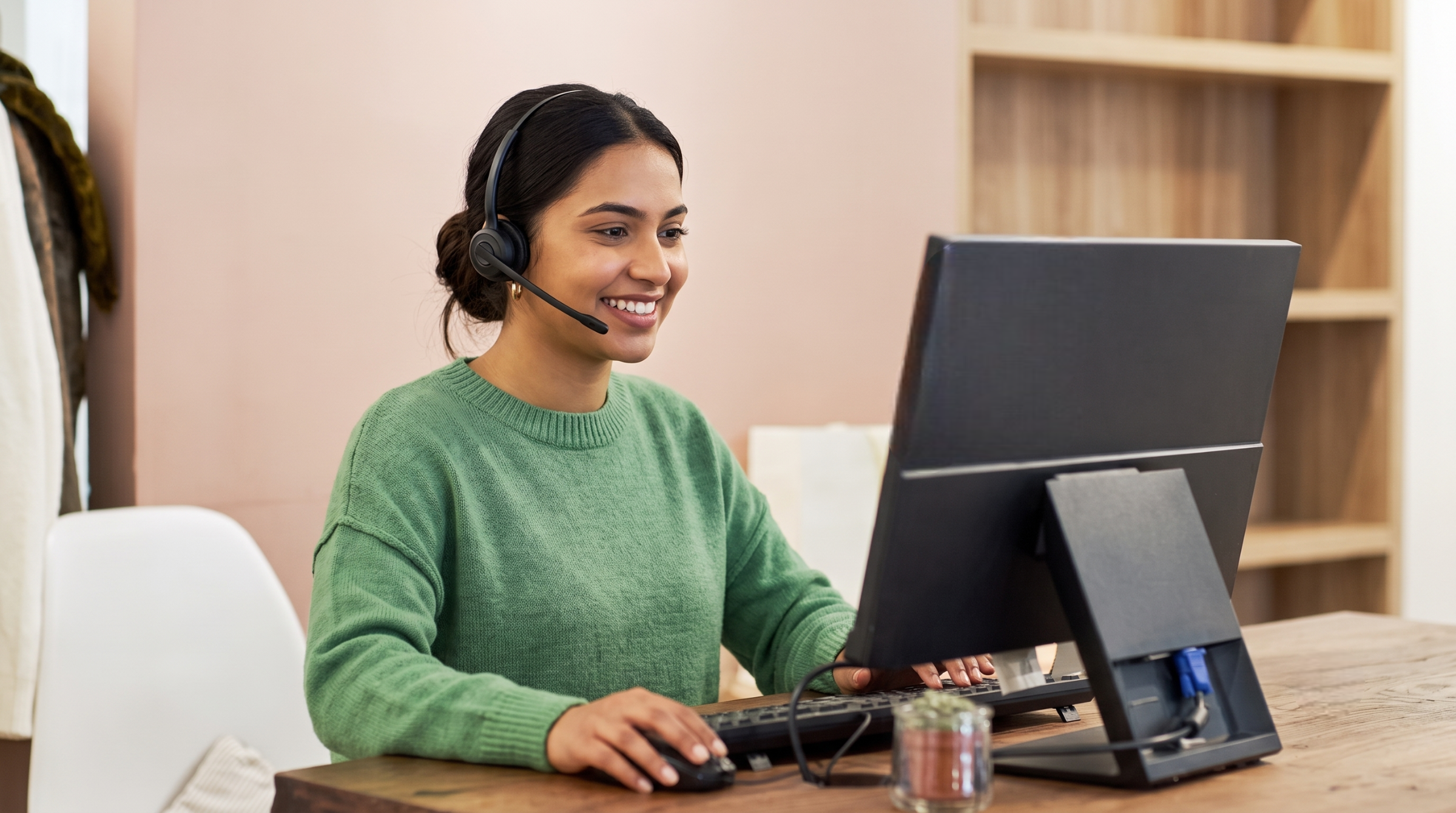 dedicated offshore customer experience officer wearing a green sweater and headset, helping customers from her computer desk.