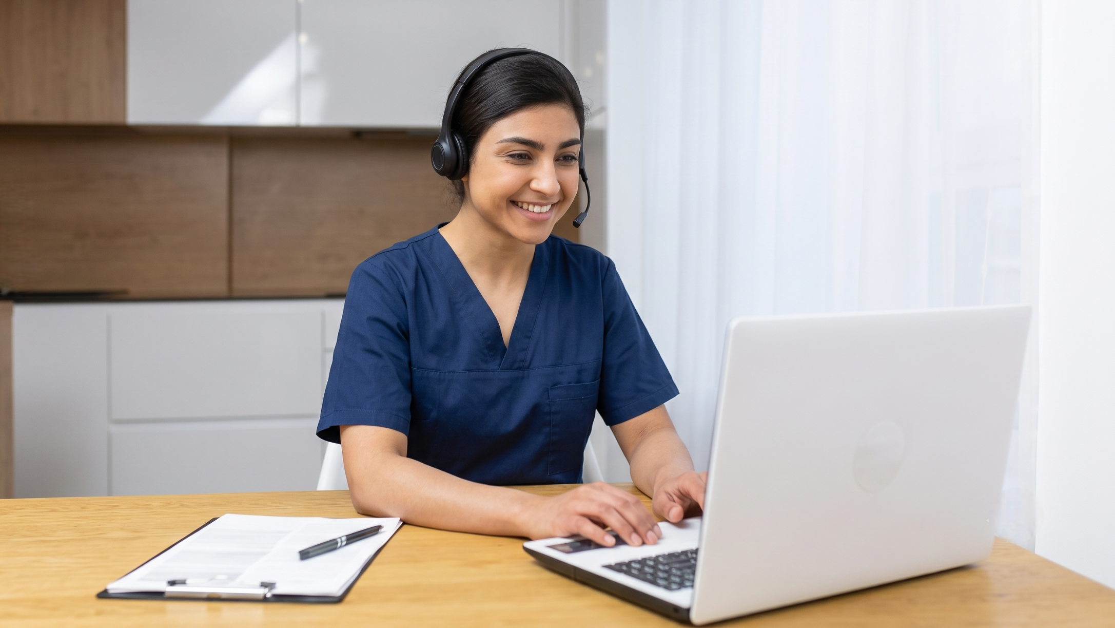 Female remote medical data entry professional in scrubs working on a laptop