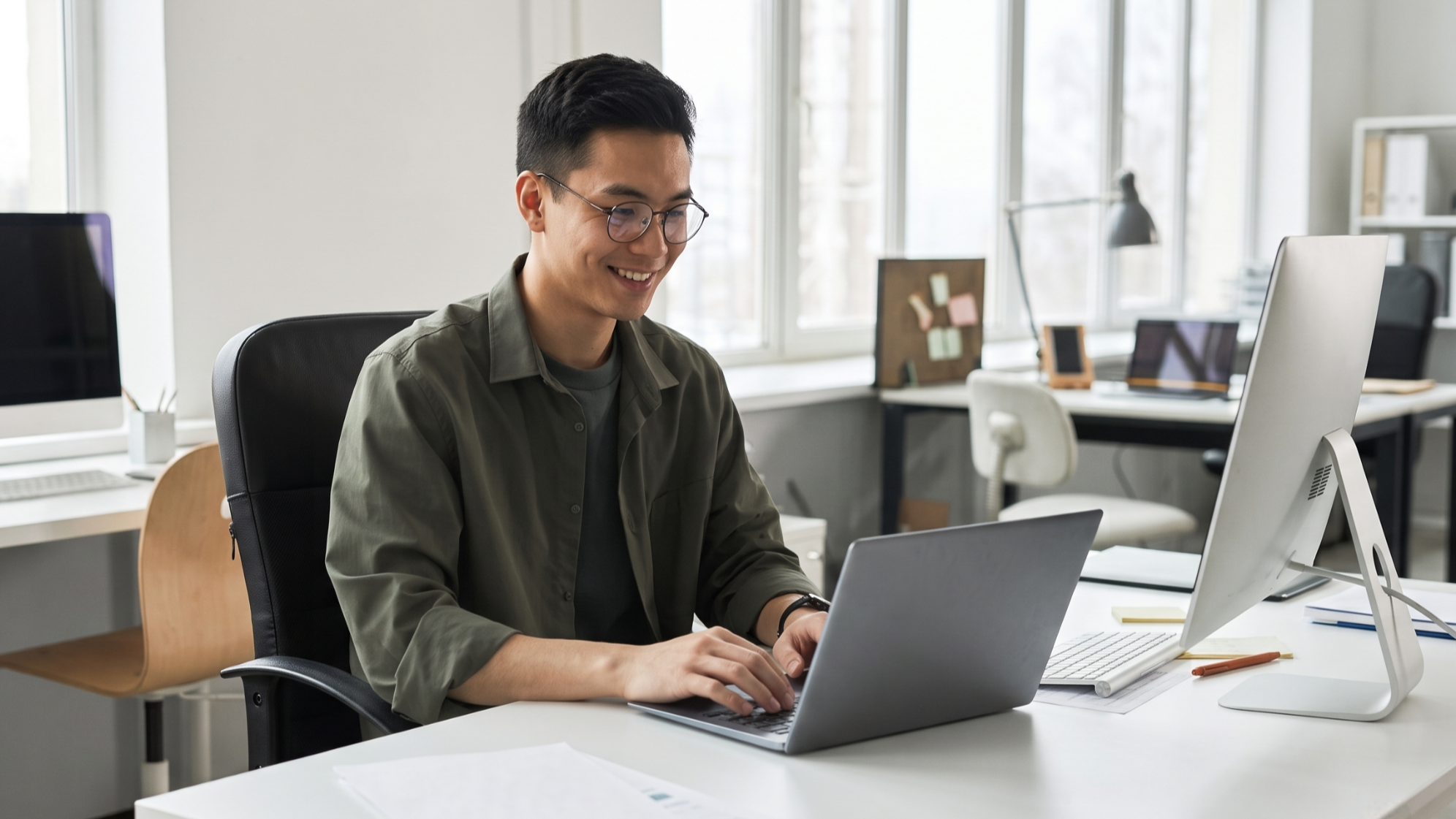 Smiling male remote soc analyst working on a laptop at his desk with large windows