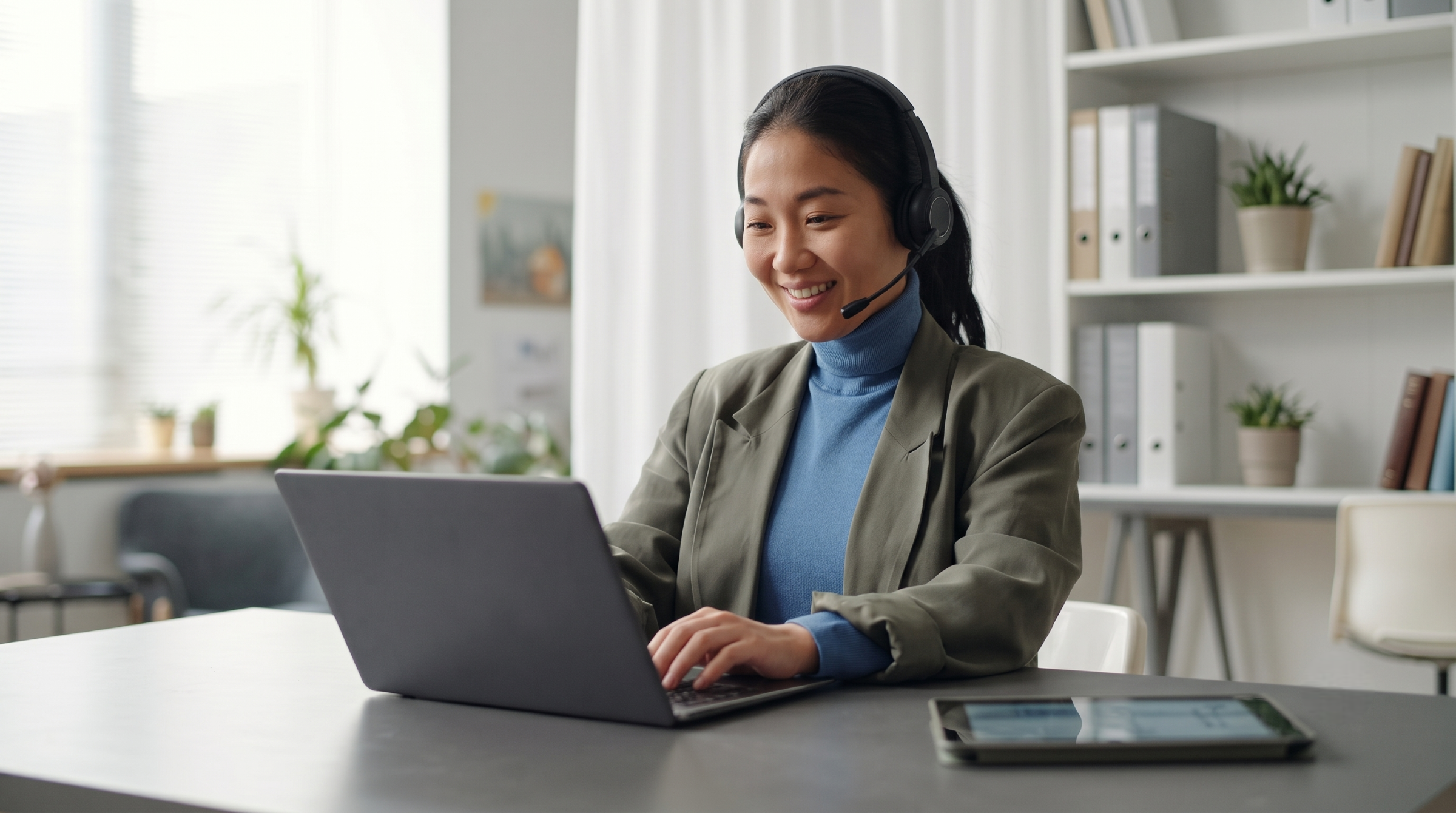 Professional Asian woman wearing a blazer and headset, working as an outsource solutions specialist at her desk