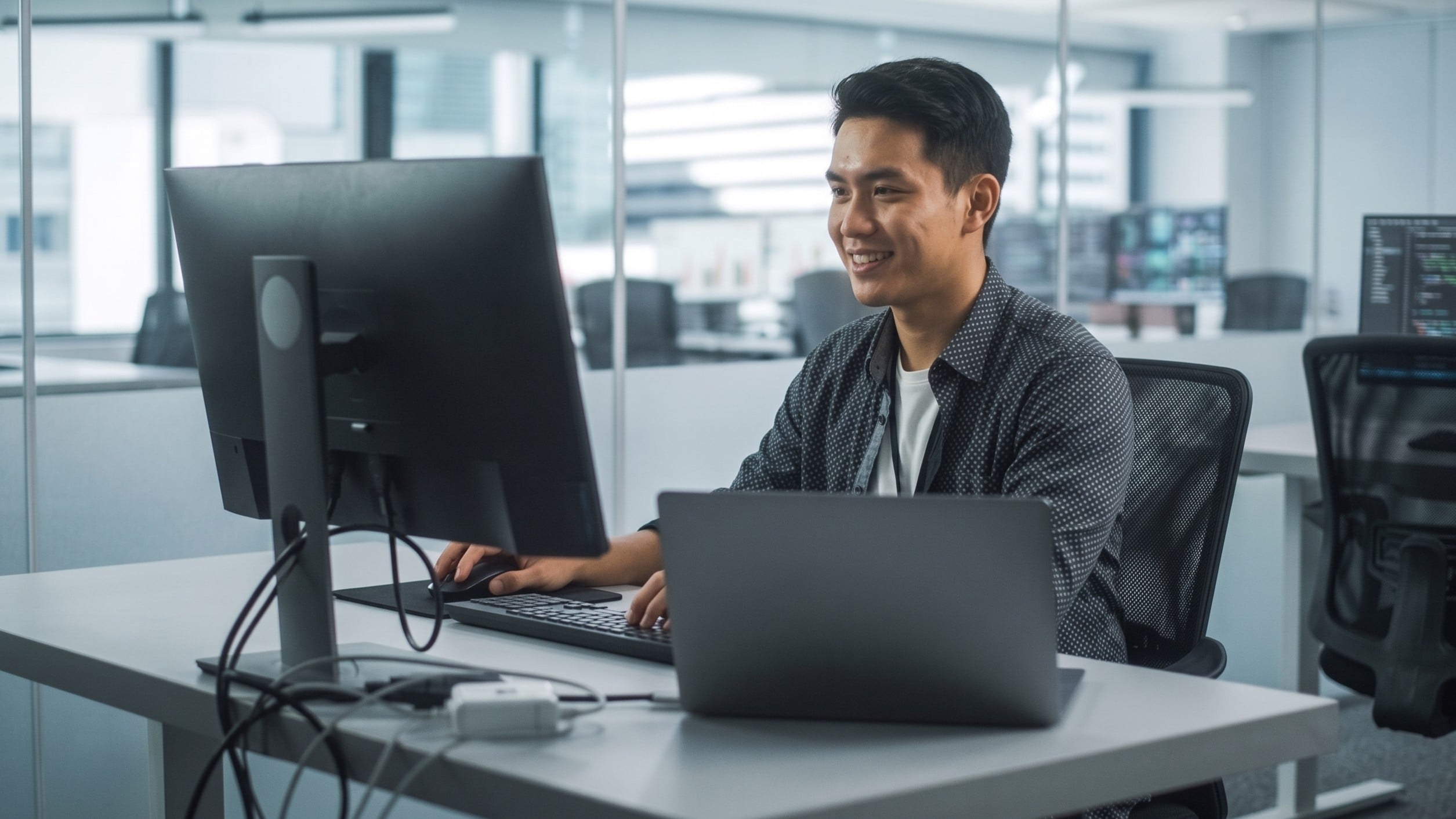 Malaysian remote AI agent manager working with a monitor and laptops