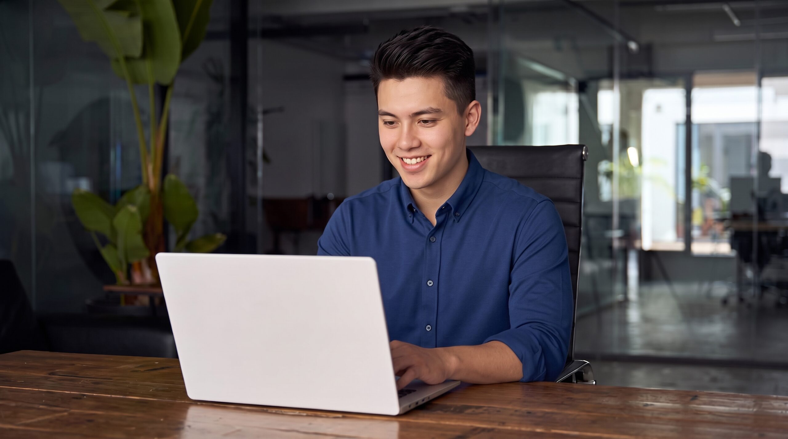 remote martech specialist working on a laptop at a wooden desk in a modern office with glass walls