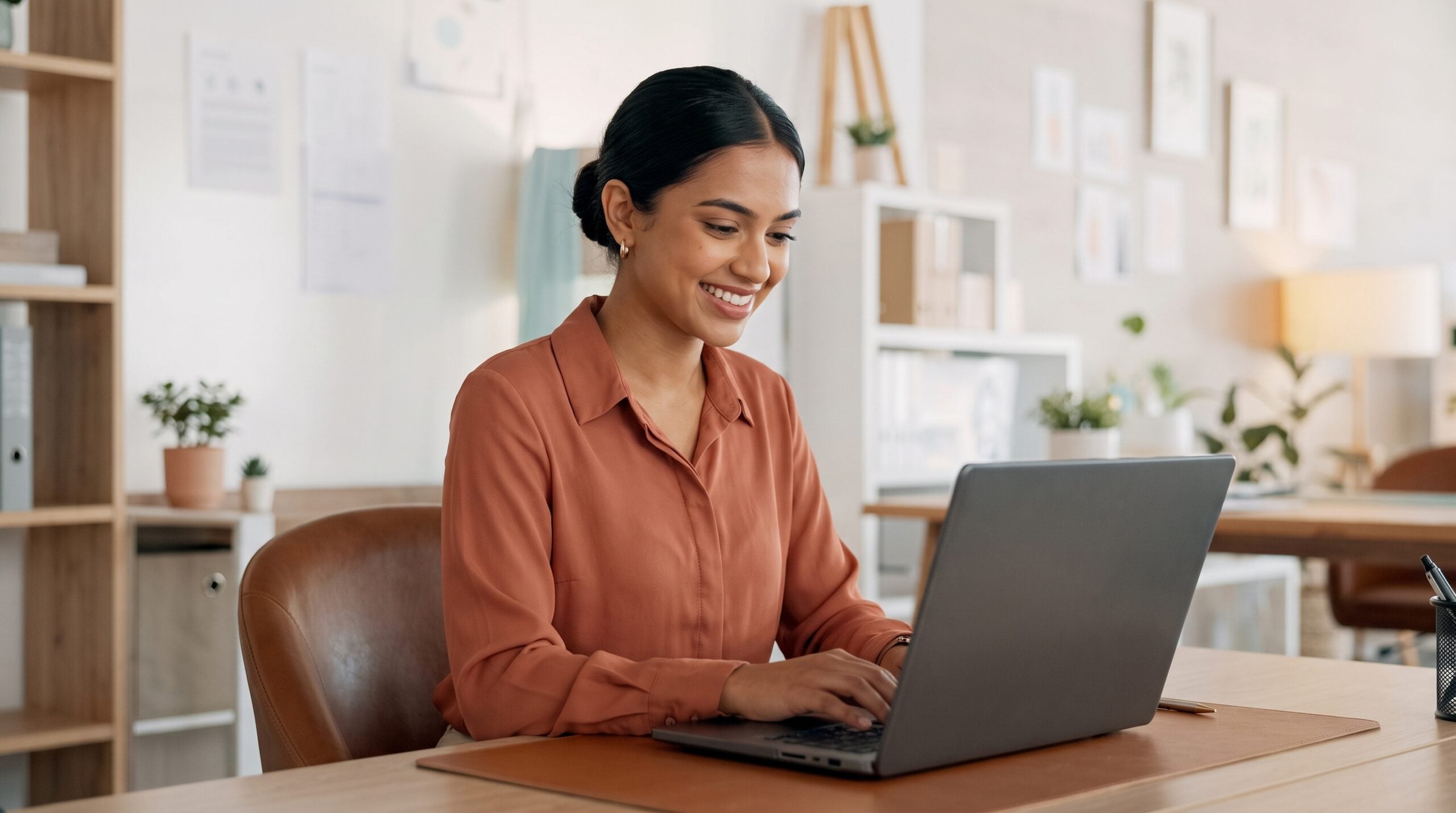 indian outsourced martech specialist works on a laptop in a cozy home office, smiling while typing on the keyboard