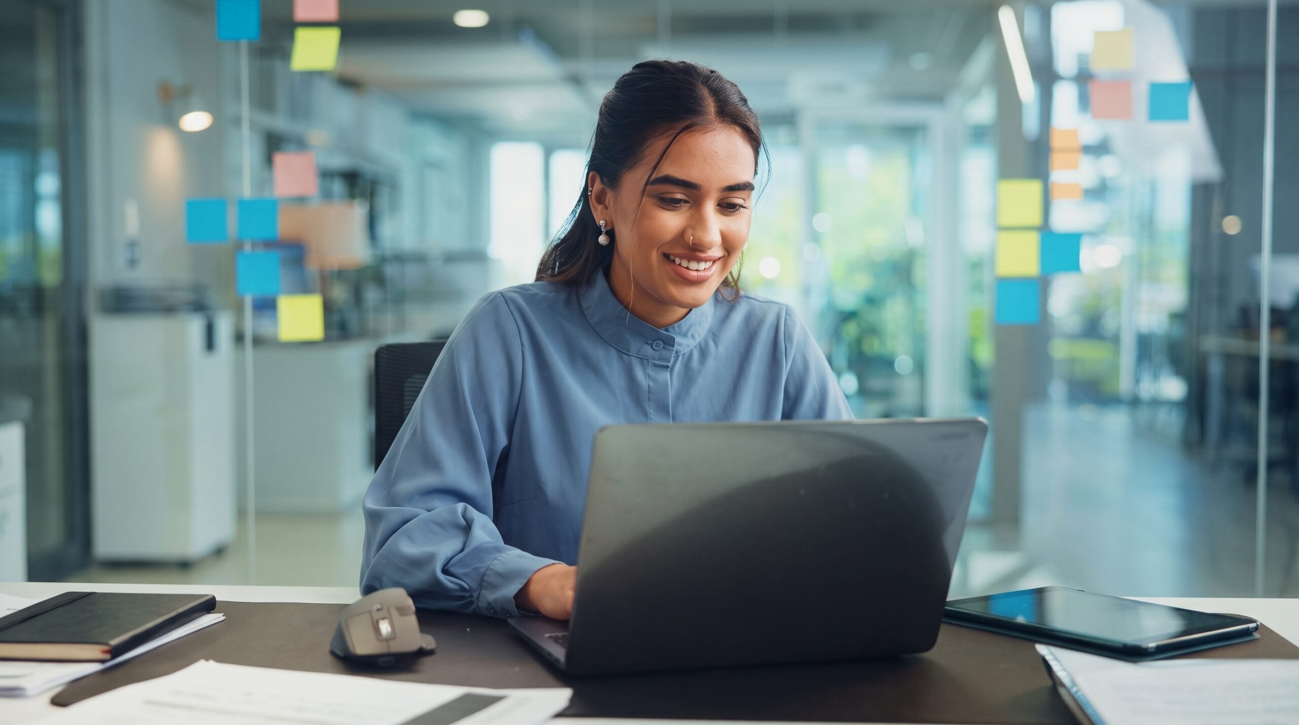 A virtual implementation manager typing on a laptop with a smile at an office desk