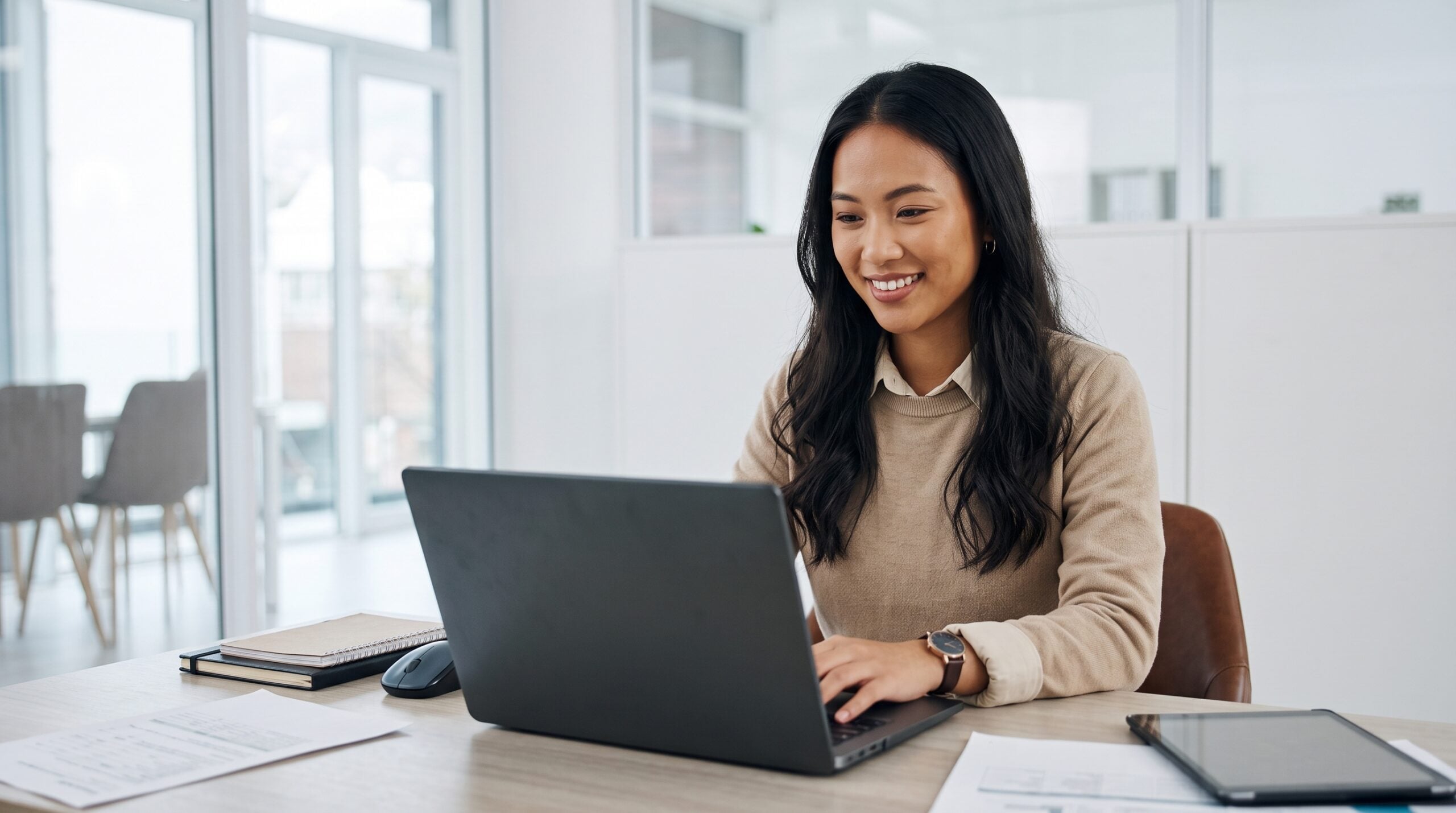 A remote implementation manager smiling as she works on a laptop at a workspace