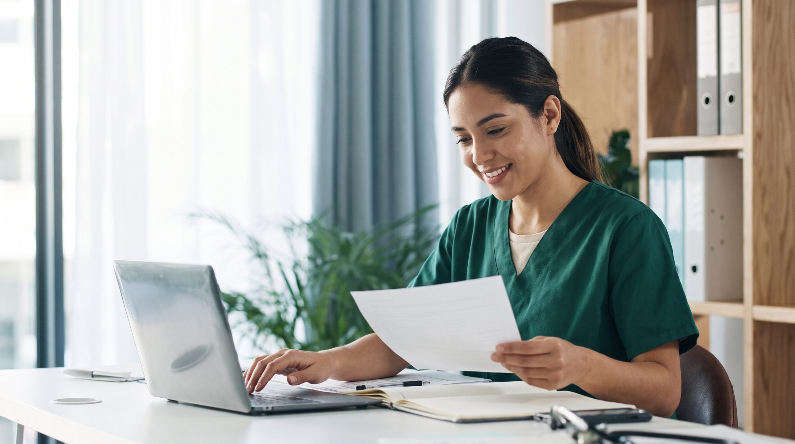 An outsourced utilization management nurse reviewing patient medical files while working on a laptop