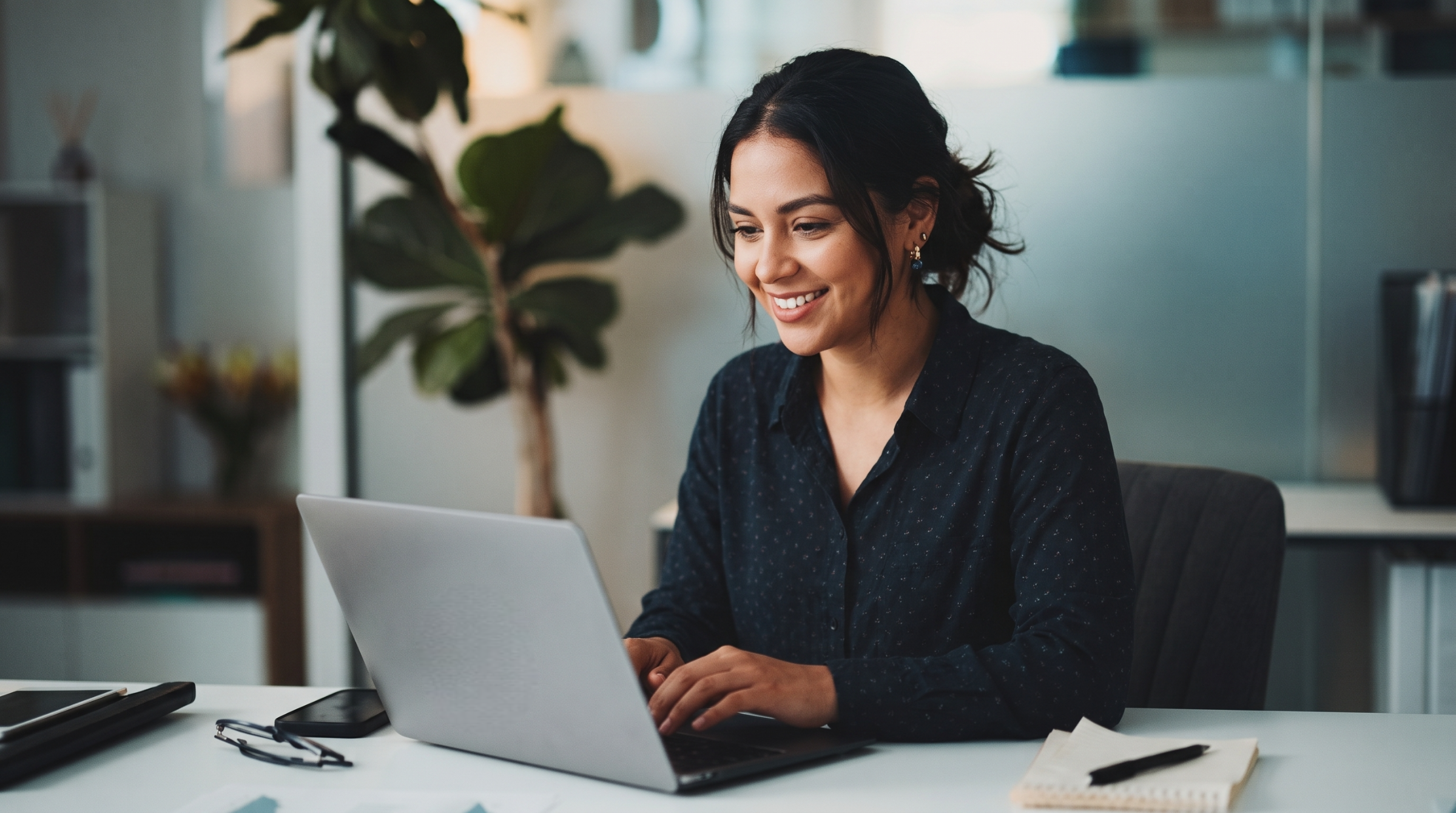 An outsourced sales engineer smiling while using a laptop in a brightly lit office setup