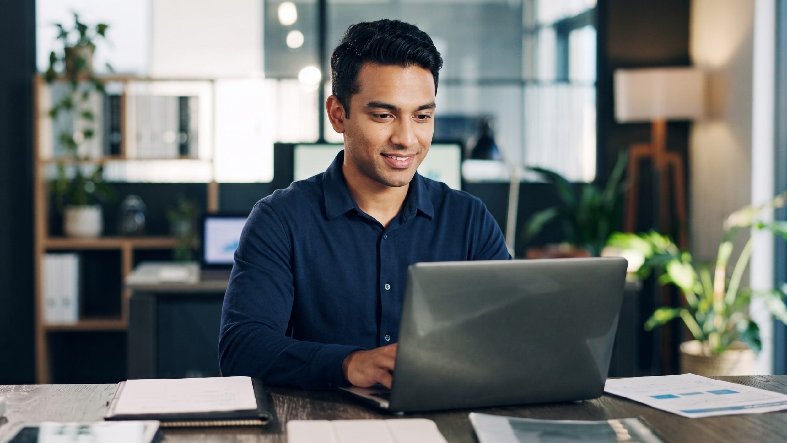 A virtual sales engineer reviewing documents and typing on a laptop at his desk