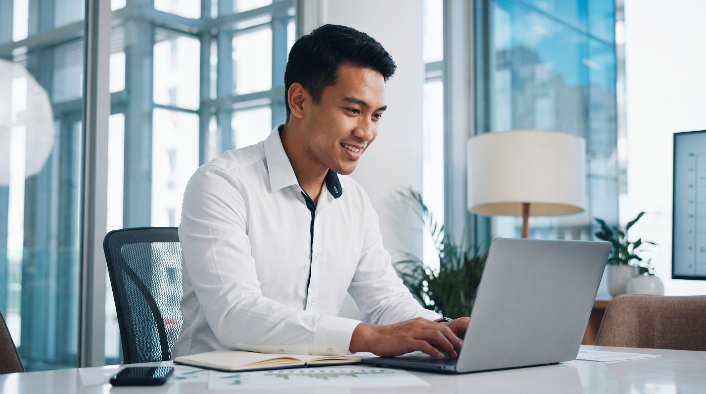 A remote sales engineer smiling while typing on his laptop at a modern office desk