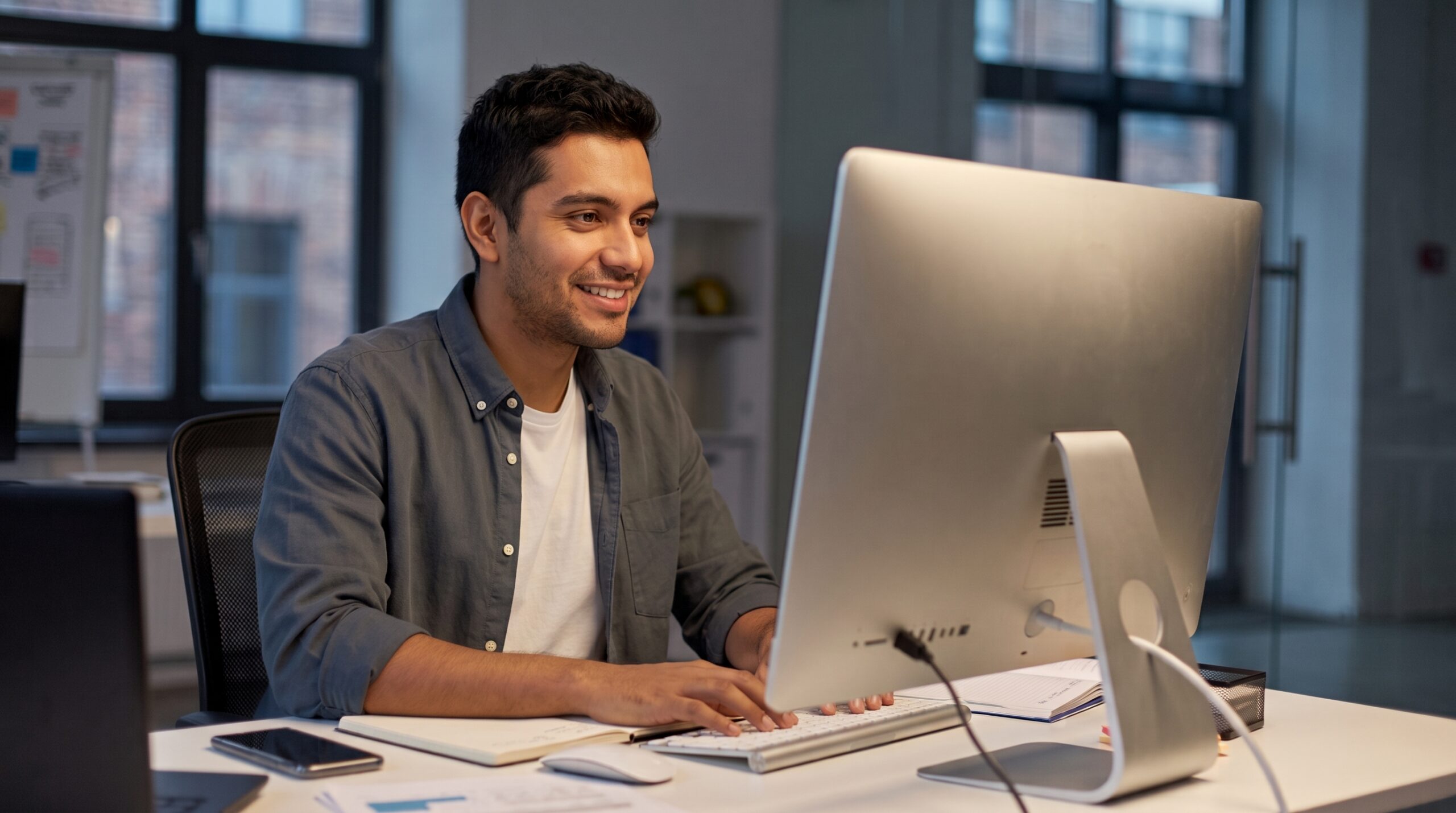 remote solutions engineer smiling as he types on a computer at a desk in an office